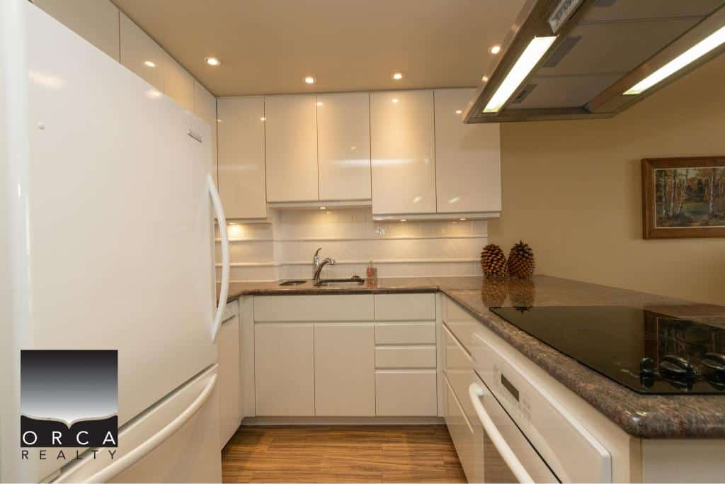 Modern kitchen with white cabinetry, stainless steel sink, and black stovetop showcasing Orca Realty Inc. services in Vancouver area.