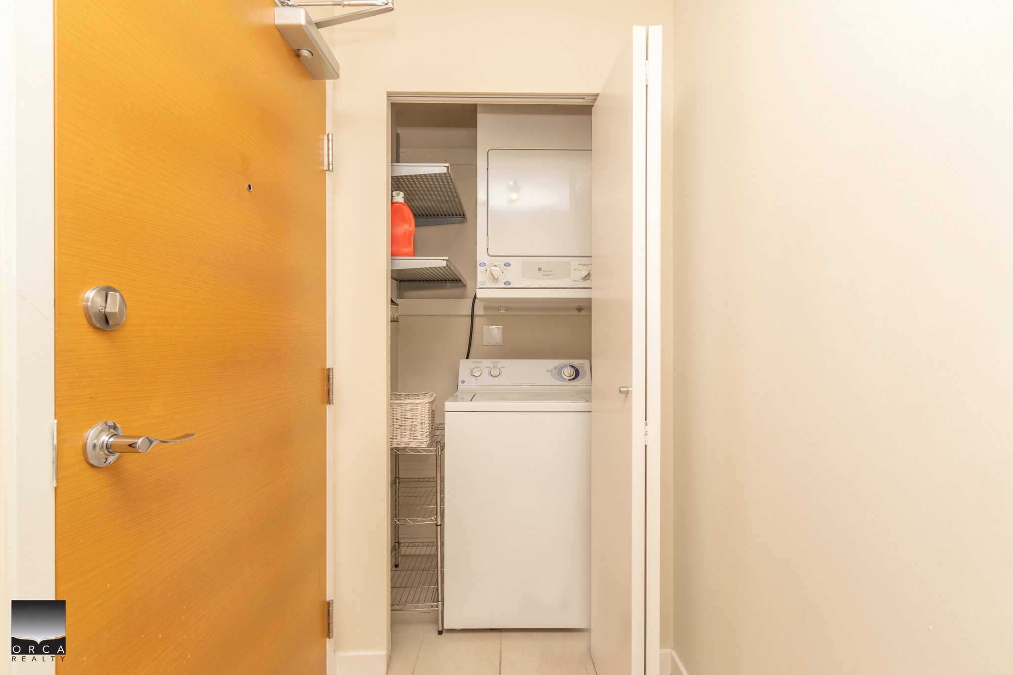 Compact laundry area with stacked washer and dryer in a modern condo, featuring built-in shelving for storage, ideal for small spaces and apartment living in the Vancouver real estate market.