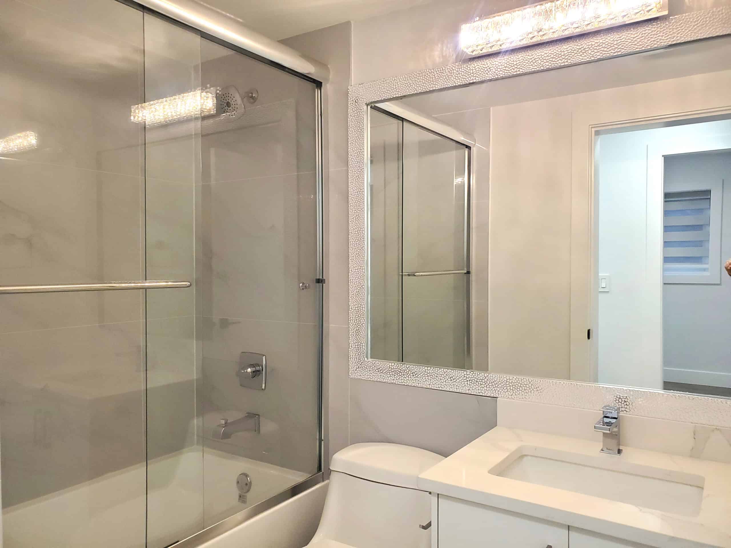 Modern bathroom with glass-enclosed shower, white vanity with integrated sink, large mirror, and neutral colour scheme, showcasing contemporary home features for Vancouver real estate.