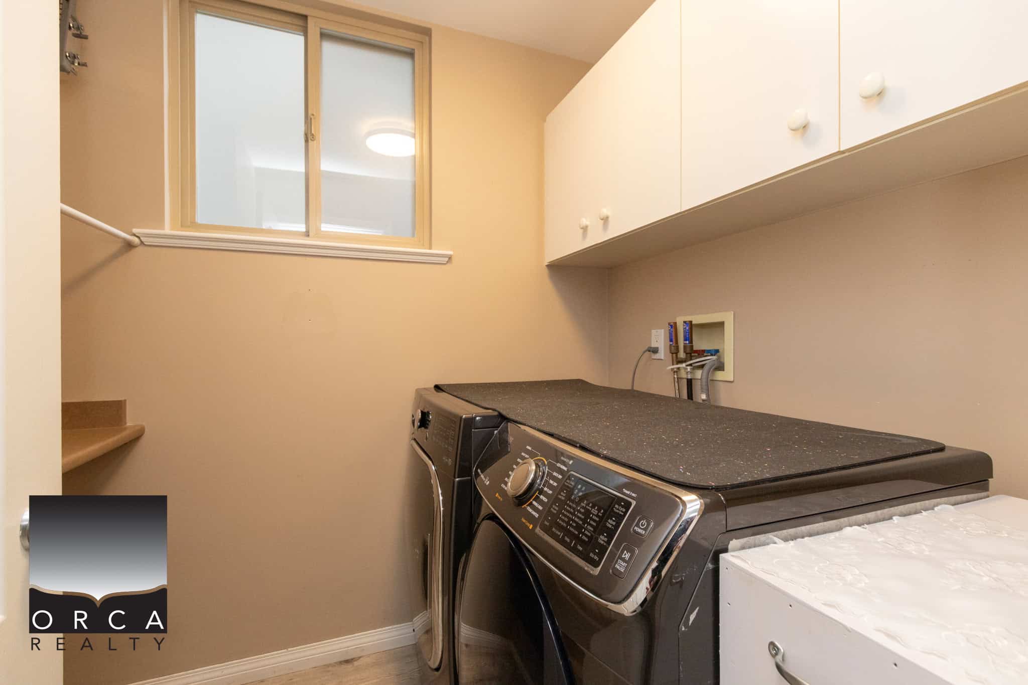 Spacious laundry room with washer and dryer, beige walls, white upper cabinets, and a small window for natural light, perfect for Vancouver housing needs.