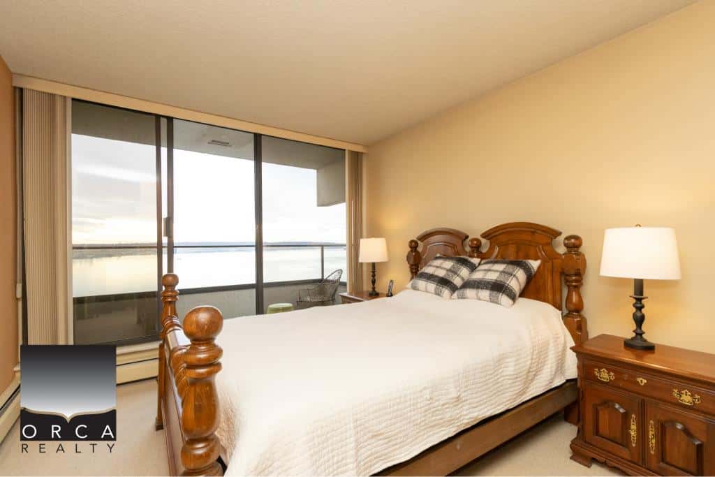 Comfortable bedroom with wooden furniture and an ocean view from the balcony in a Vancouver Island property listed by Orca Realty.