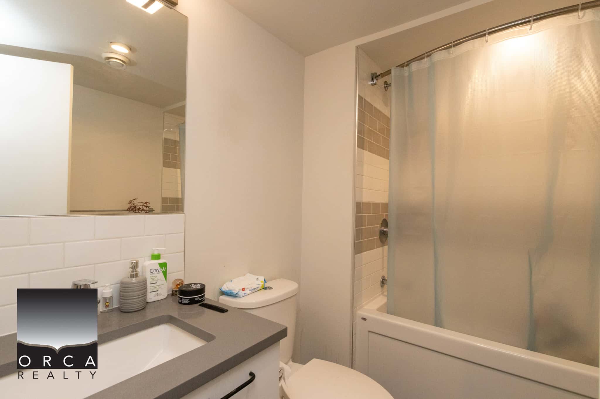 Bright modern bathroom featuring a sleek vanity with a large mirror, a toilet, and a bathtub with a frosted shower curtain, ideal for Toronto and Vancouver real estate listings.