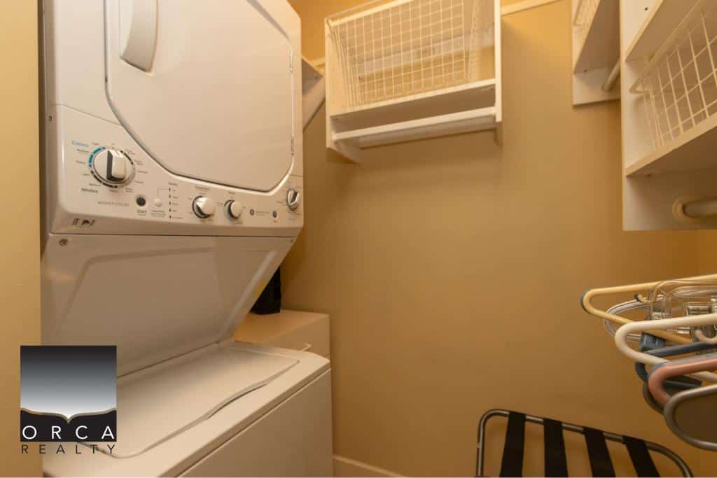 Compact laundry room with stacked washer and dryer units in a modern home, featuring organized shelving and storage solutions for convenient laundry management.
