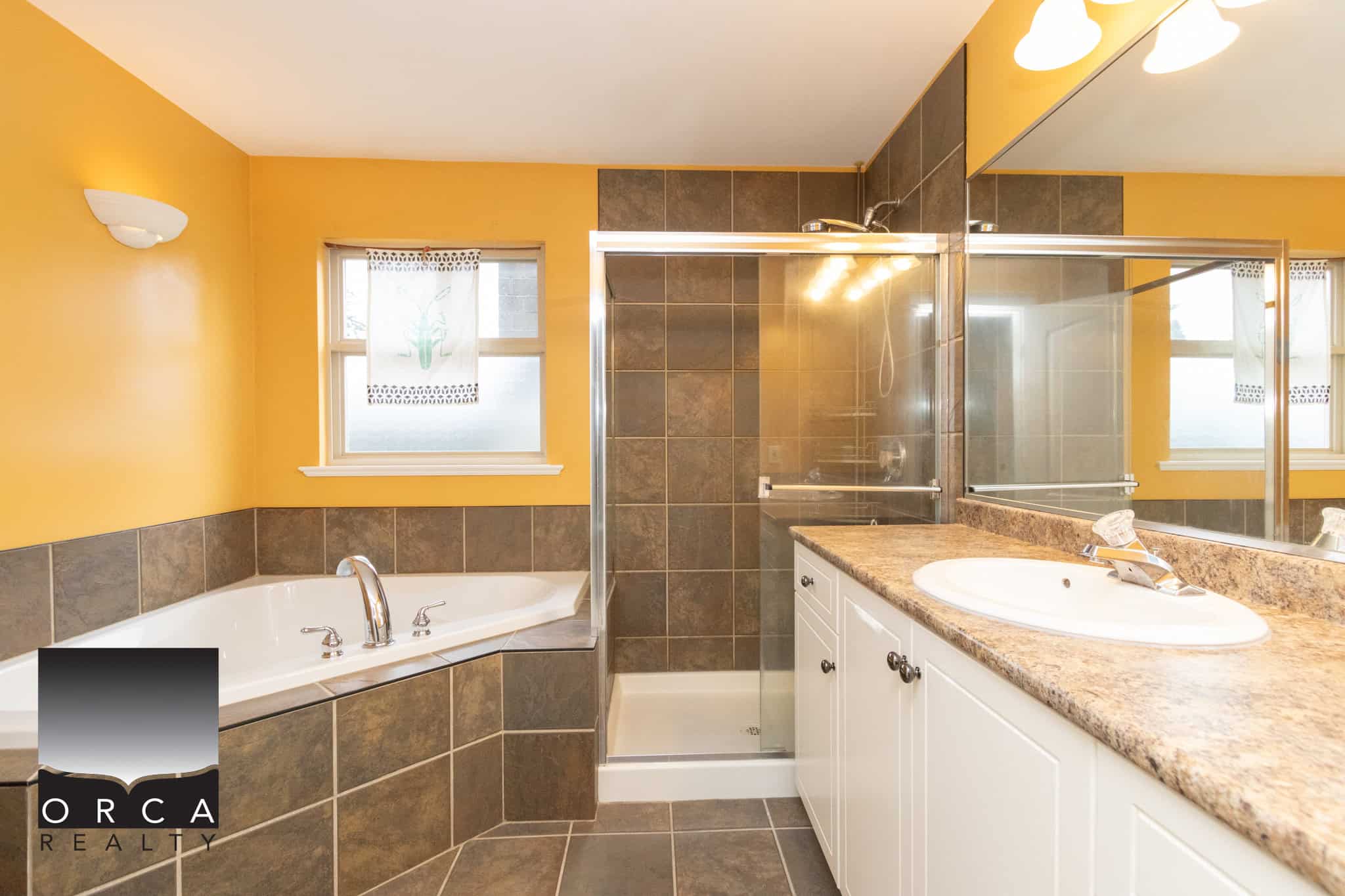 Bright yellow bathroom with modern shower stall, bathtub, and vanity featuring granite countertop and white cabinetry, perfect for Vancouver Island homeowners.