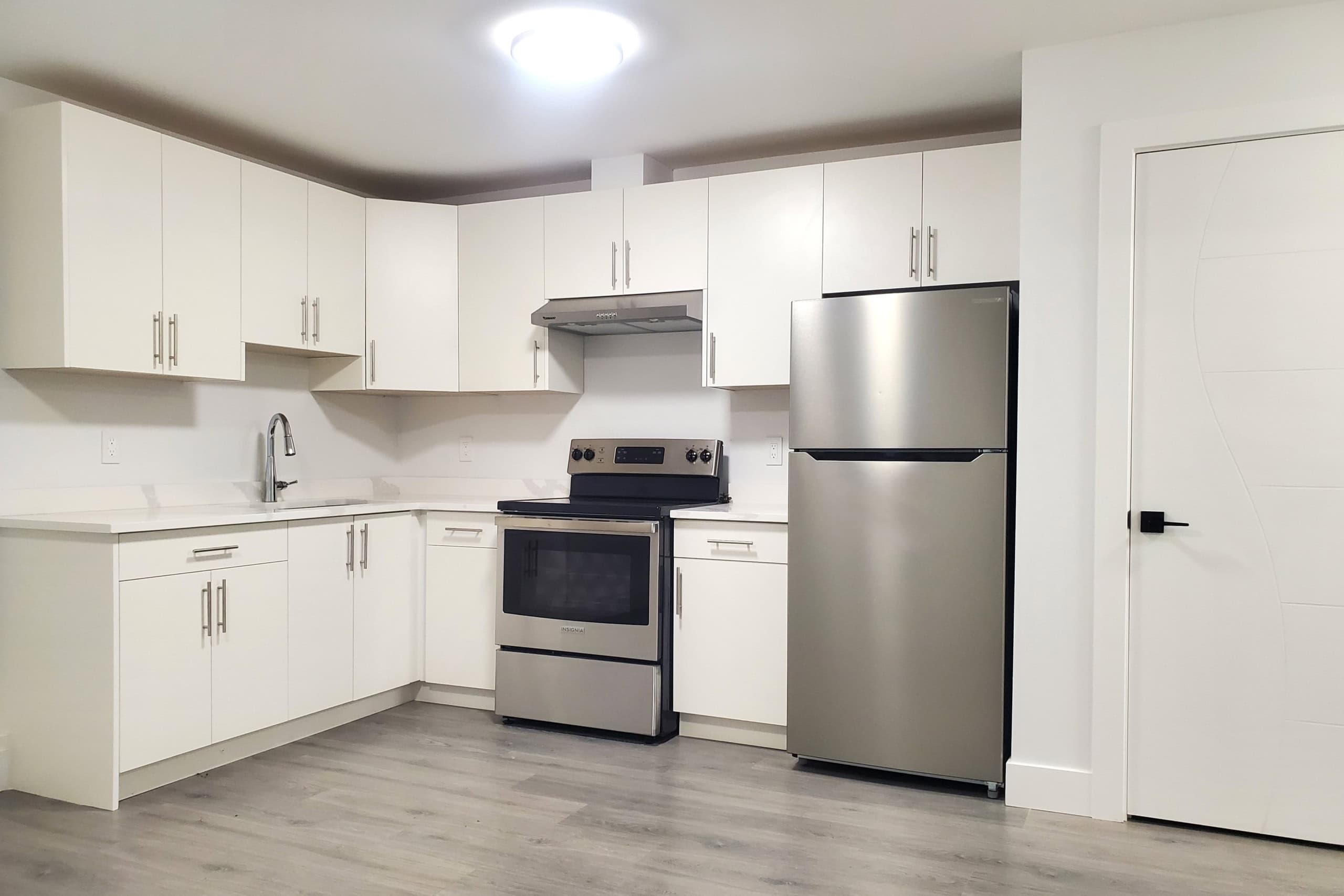 2 Bright modern kitchen with white cabinets, stainless steel appliances including a refrigerator and stove, sleek countertops, and light wood flooring, part of Orca Realty Inc. property listings.