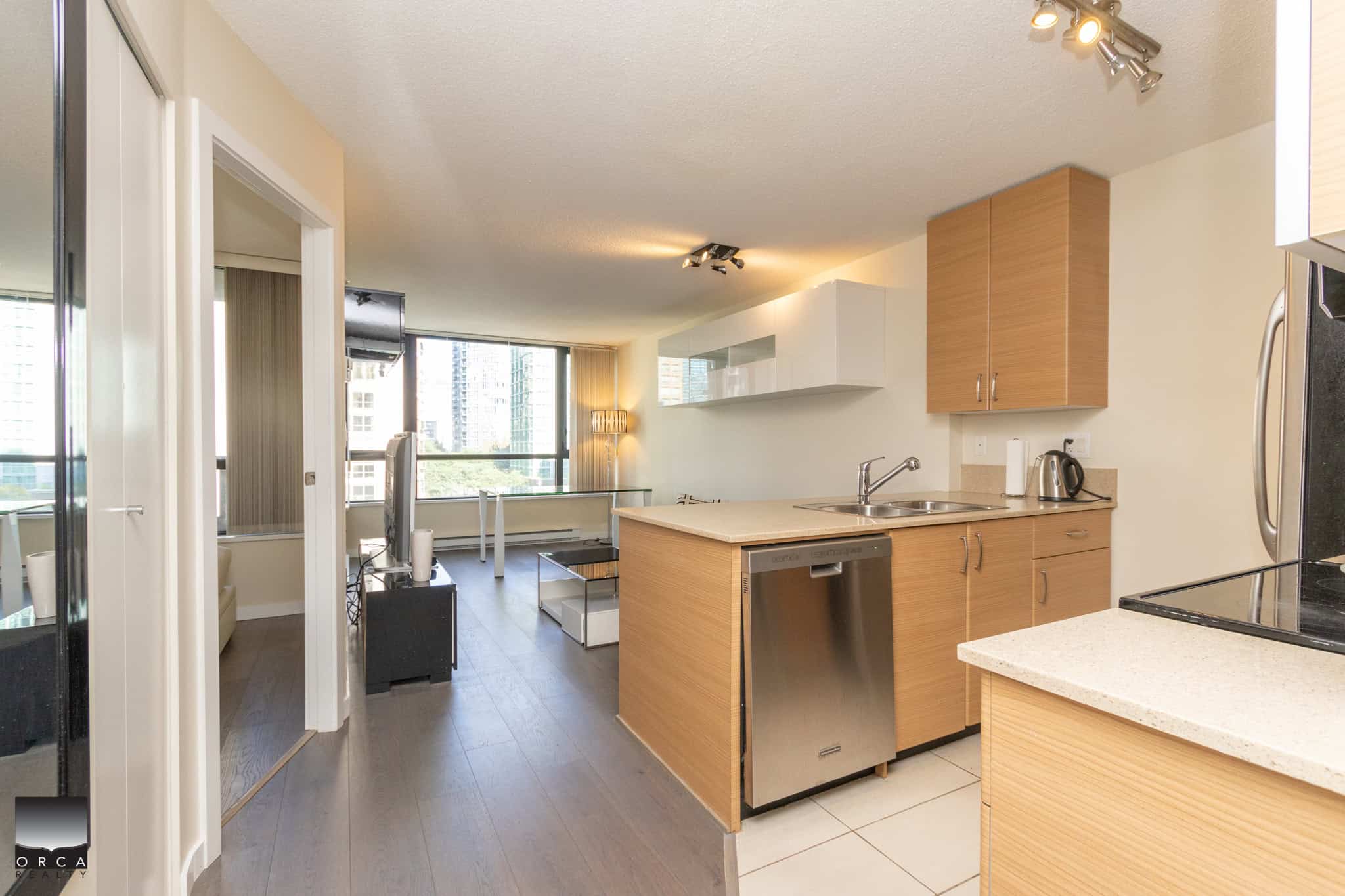 Bright open-concept kitchen and living area in downtown Vancouver condominium, featuring modern appliances, ample natural light, and stylish wood cabinetry. Ideal for urban living and investment.