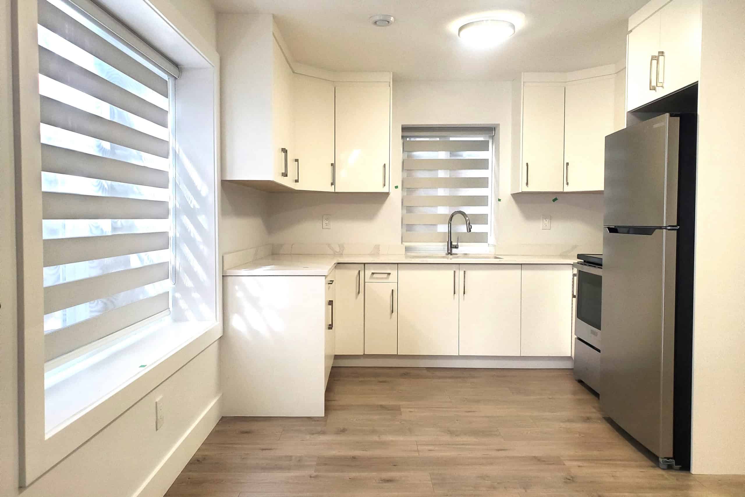 Bright modern kitchen with white cabinetry and stainless steel appliances, featuring natural light from windows with zebra blinds, ideal for Vancouver Island real estate listings.