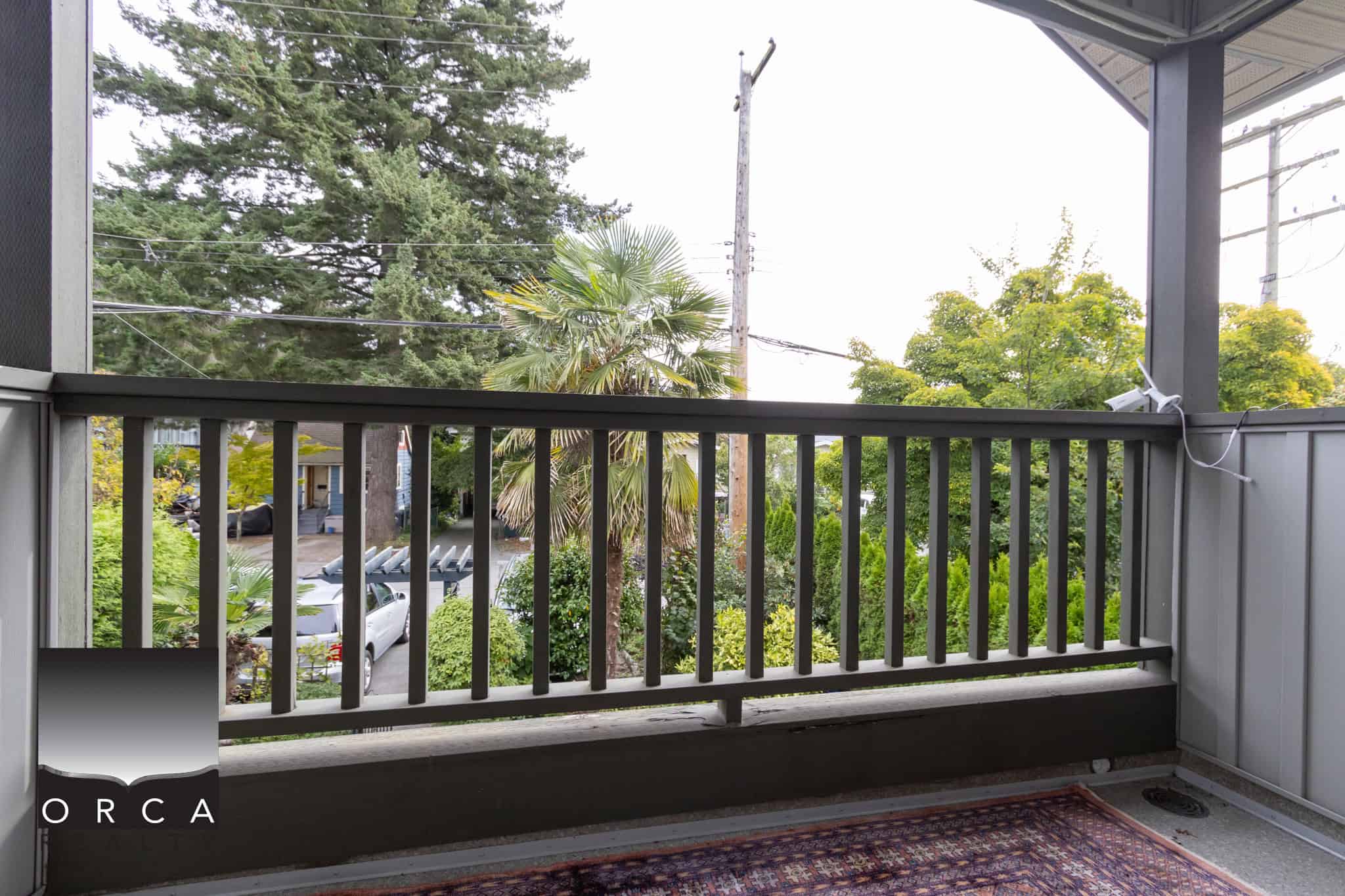 Bright balcony with wooden railing overlooking lush green trees and neighboring houses in a Vancouver area home, ideal for outdoor relaxation and enjoying nature.
