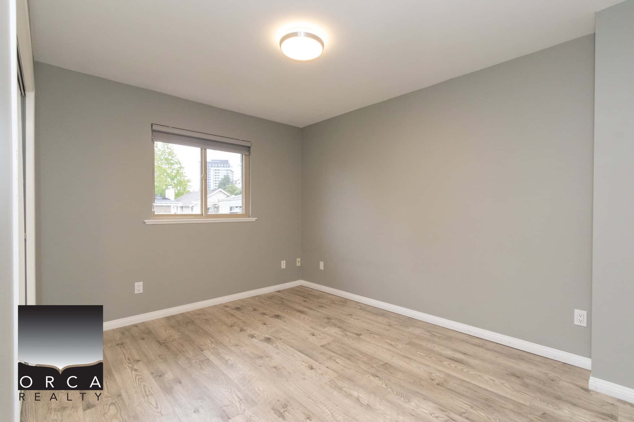 Bright unfurnished bedroom with large window, neutral grey walls, light wood flooring, ideal for Vancouver real estate listings and residential property marketing.