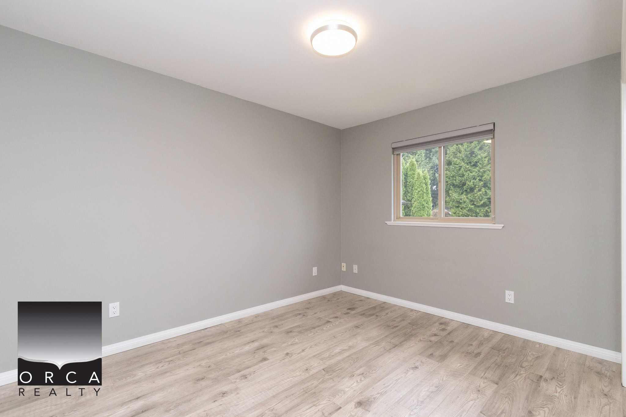 Bright and spacious empty bedroom with large window, neutral wall color, and modern flooring at Orca Realty Inc., showcasing Vancouver Island's premier real estate services.