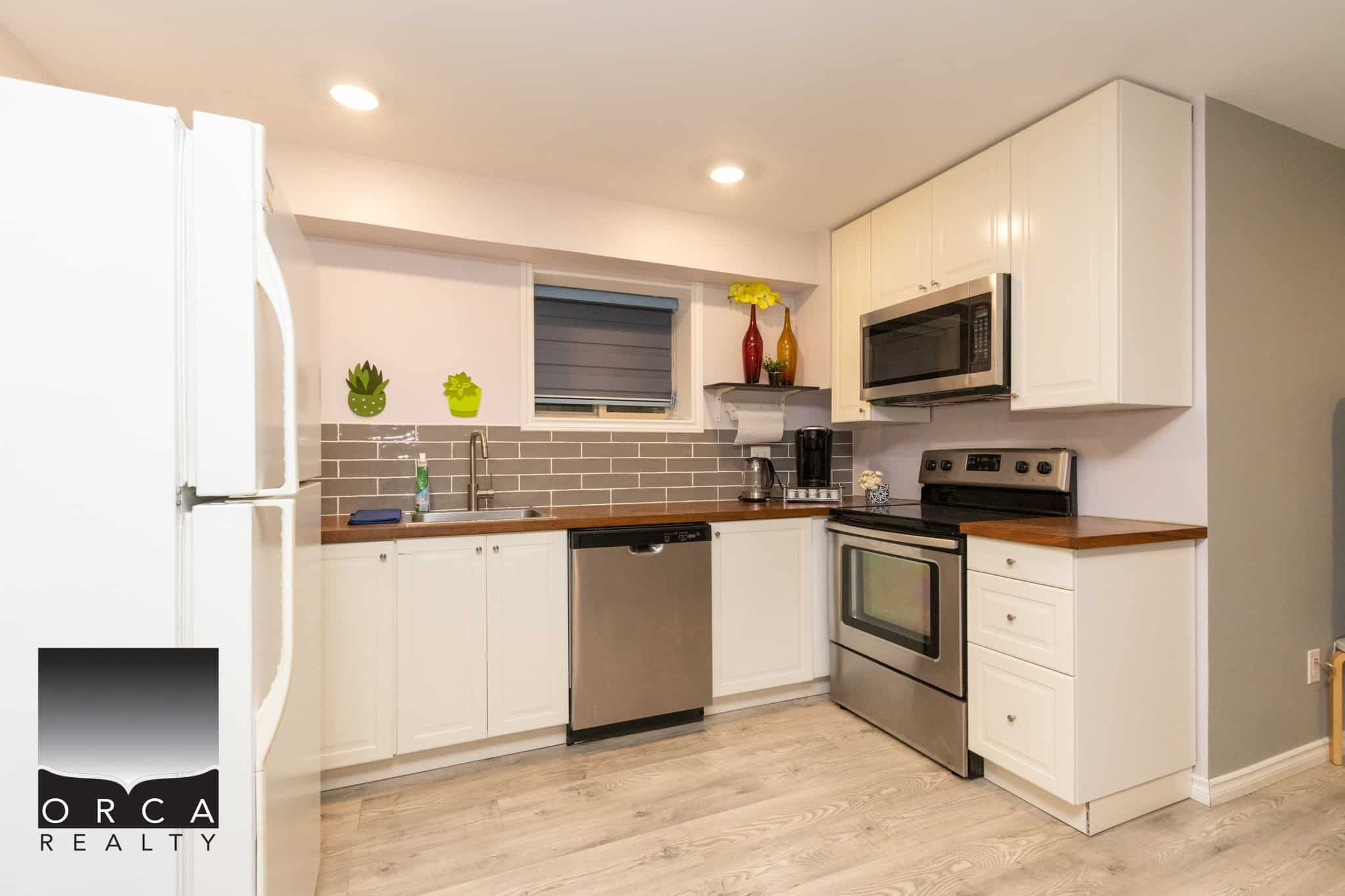Bright modern kitchen with stainless steel appliances, white cabinetry, and a stylish grey subway tile backsplash, perfect for Vancouver Island real estate buyers.