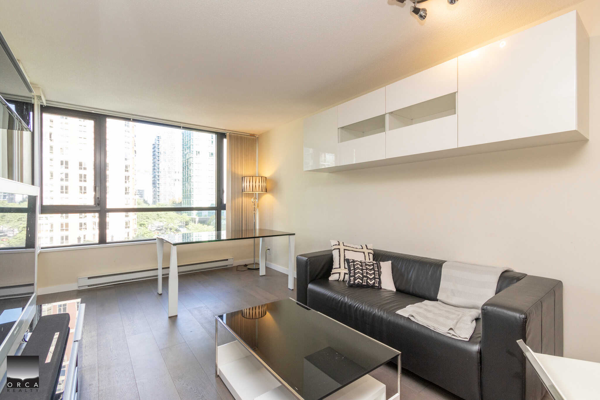Modern Vancouver city view condo living room with large windows, contemporary black leather sofa, and stylish decor in a downtown high-rise building - Orca Realty Inc.