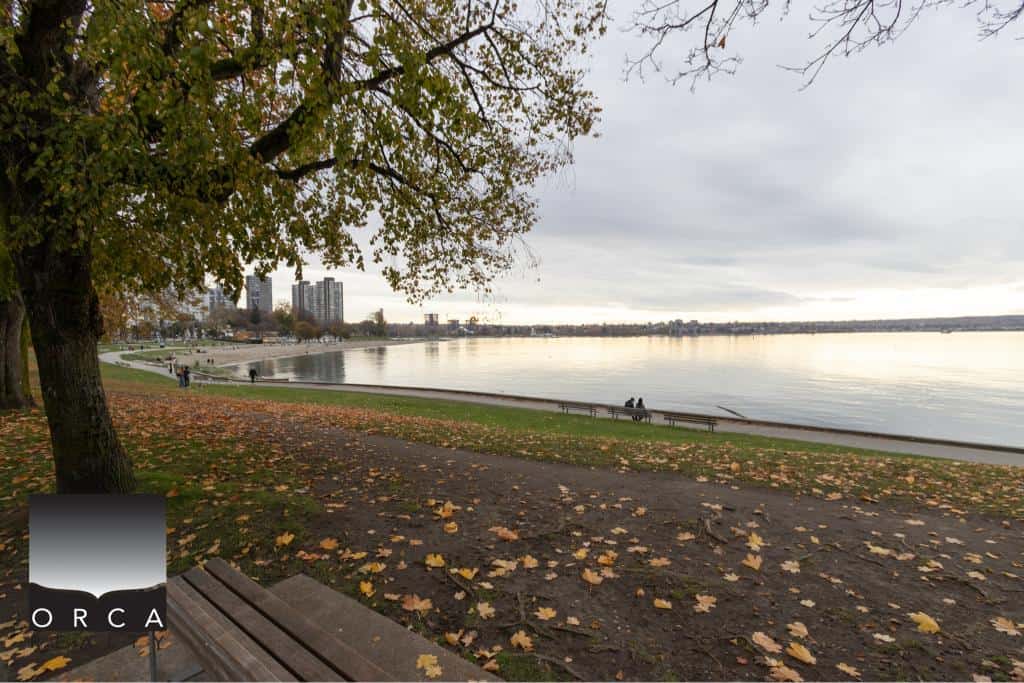 Serene lakeside park with autumn leaves, tranquil water, and city skyline in the background, perfect for relaxing and enjoying nature in Vancouver, BC.