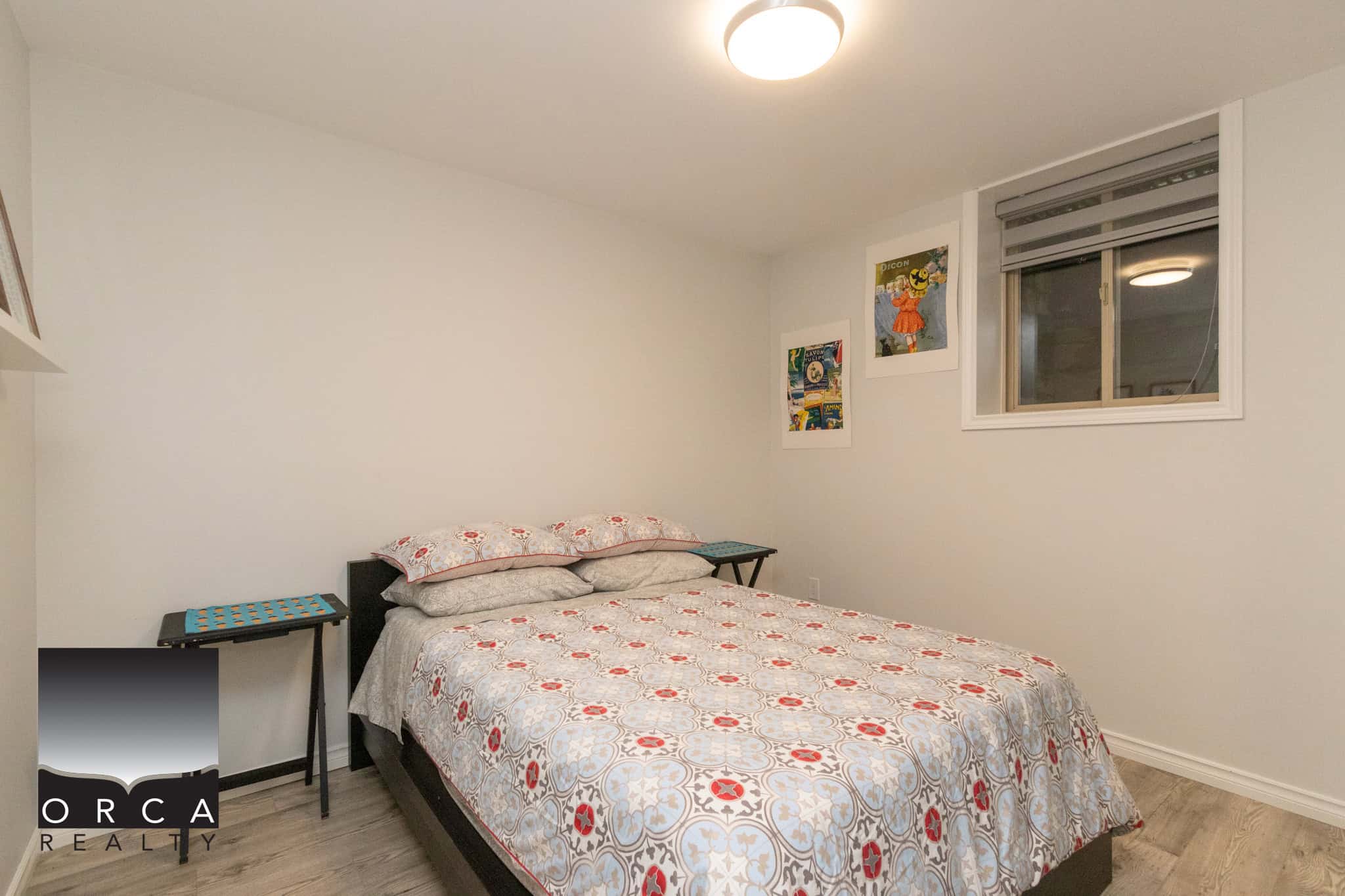 Cozy bedroom with white walls, modern decor, and large window, ideal for Vancouver Island living, featuring fresh paint and hardwood floors. Perfect for real estate listings or property showcases.