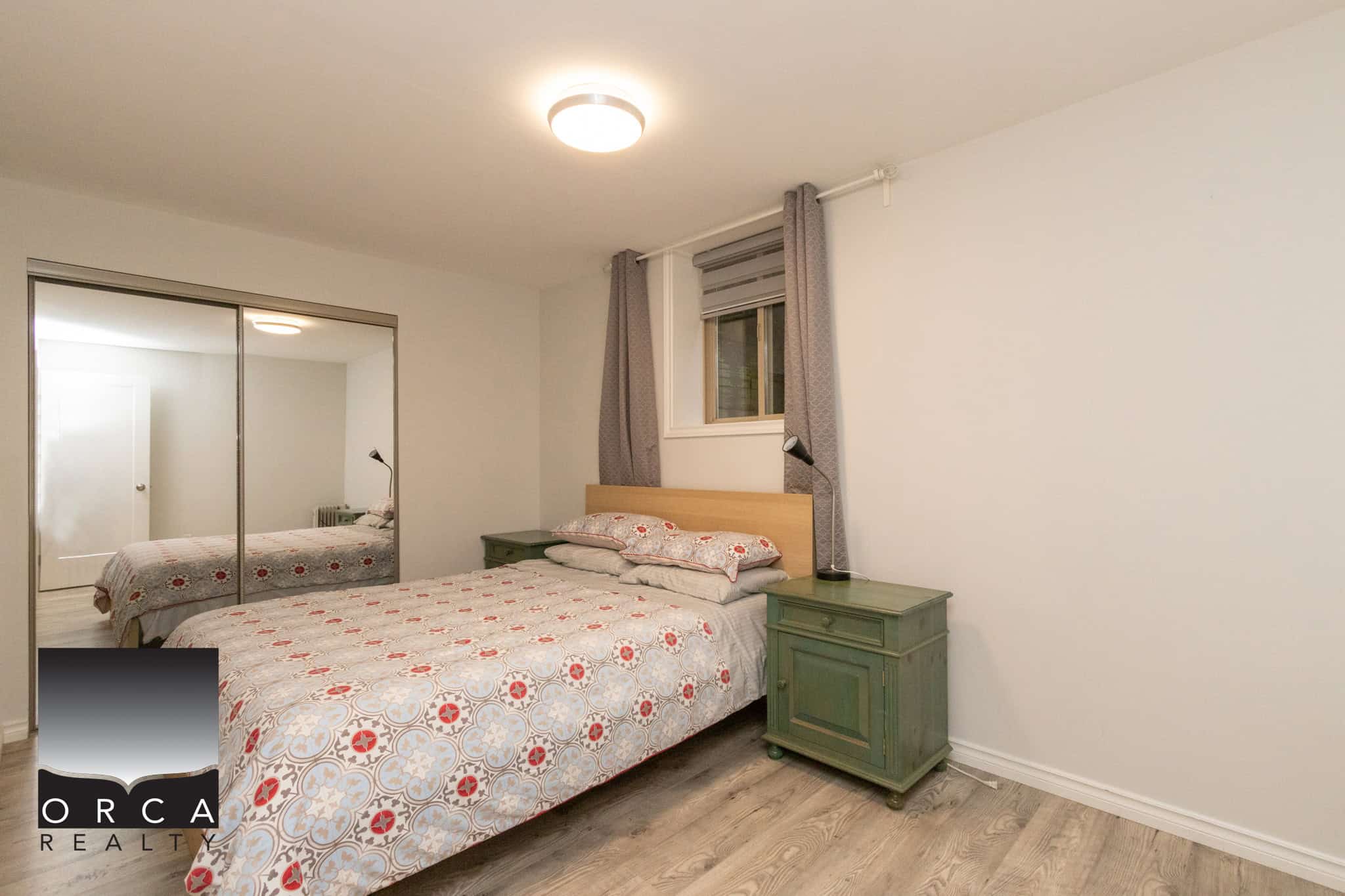 Cozy bedroom with green nightstands, floral bedding, and a window with curtains, showcasing a modern, minimalist design perfect for Vancouver real estate listings.