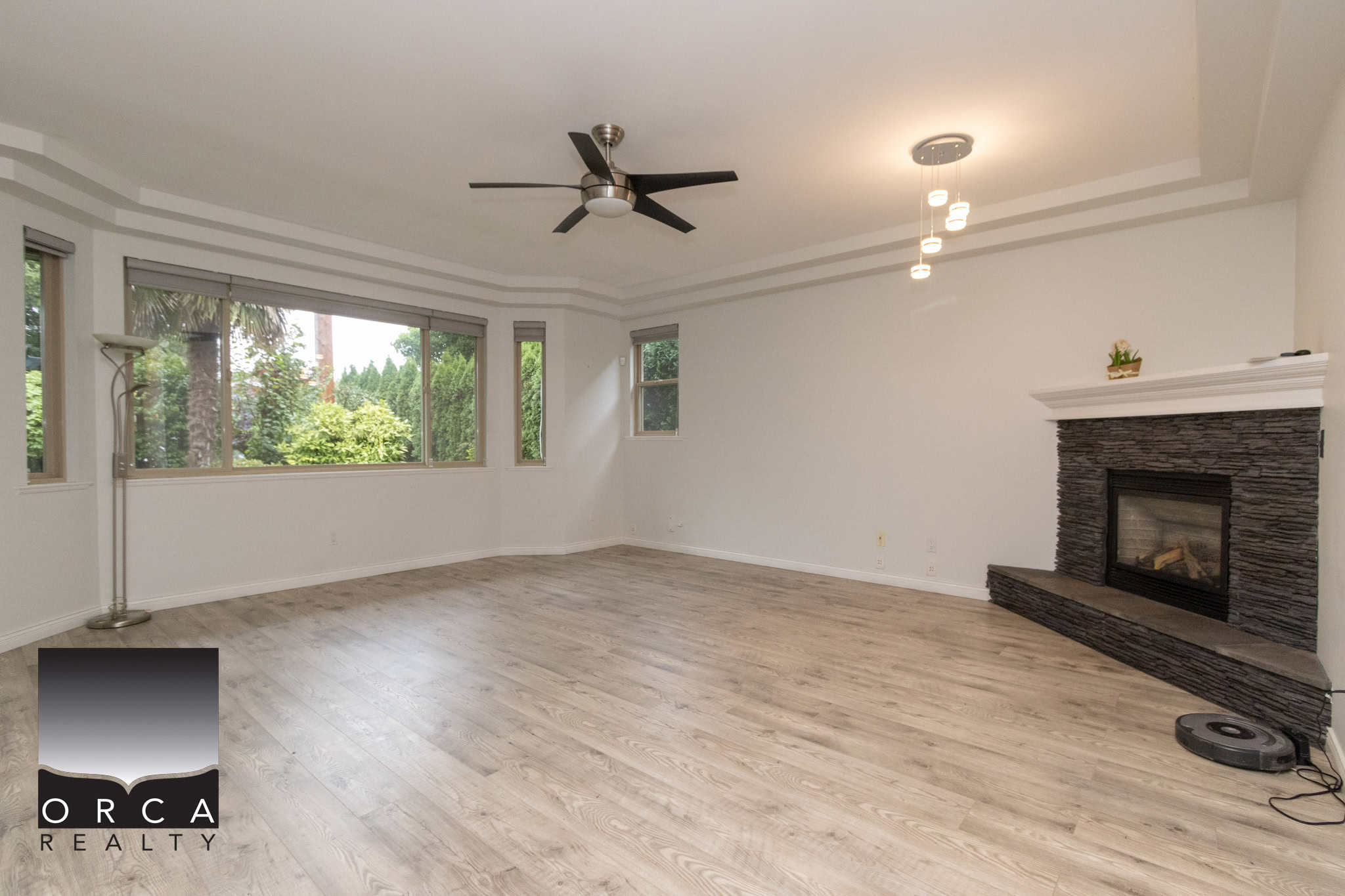 Spacious living room with large windows, modern ceiling fan, fireplace, and light wood flooring, ideal for family gatherings and entertaining in British Columbia homes.