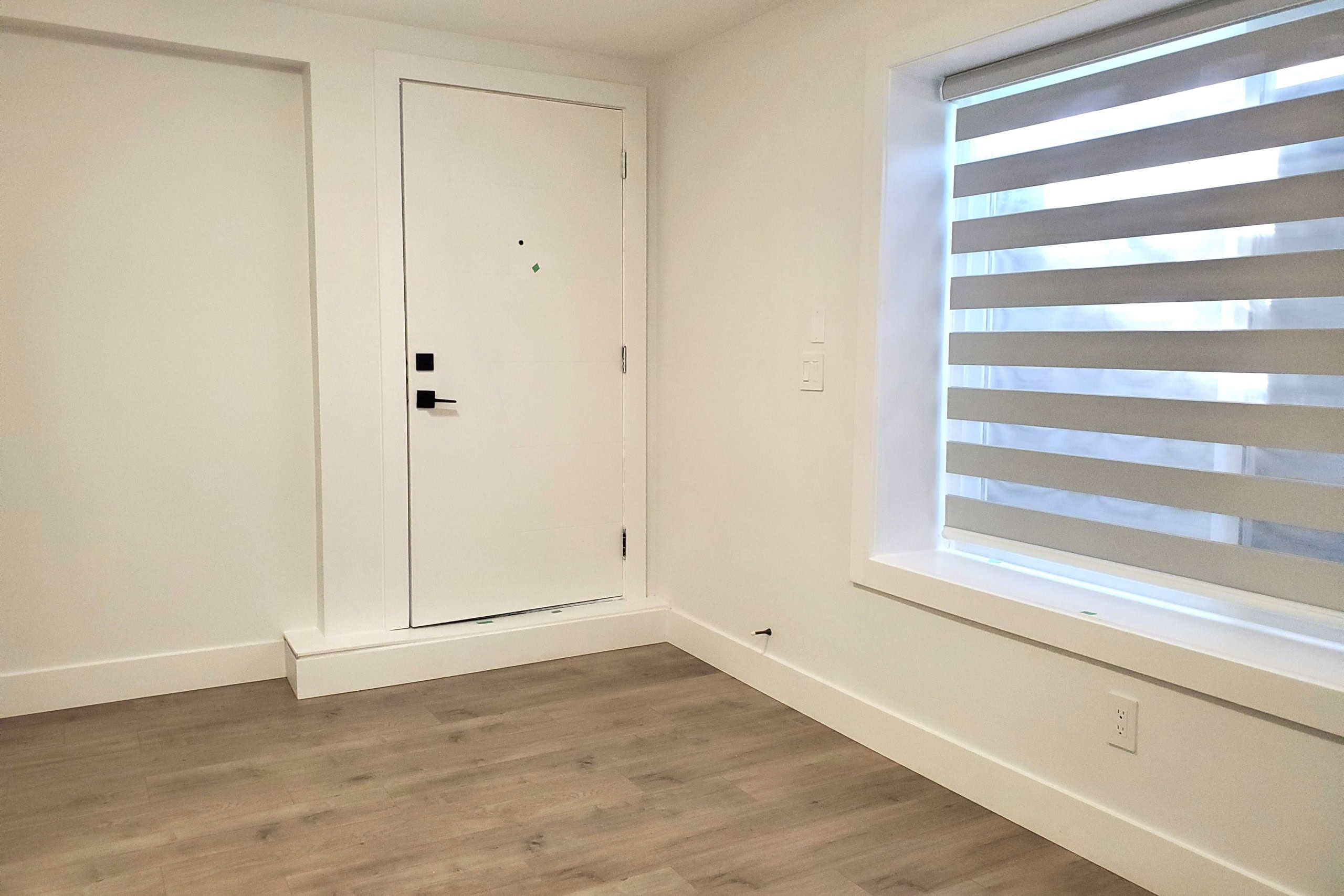 Modern minimalist interior of a rental or condo unit showing a white door and large window with horizontal blinds, ideal for Vancouver real estate listings by Orca Realty Inc.