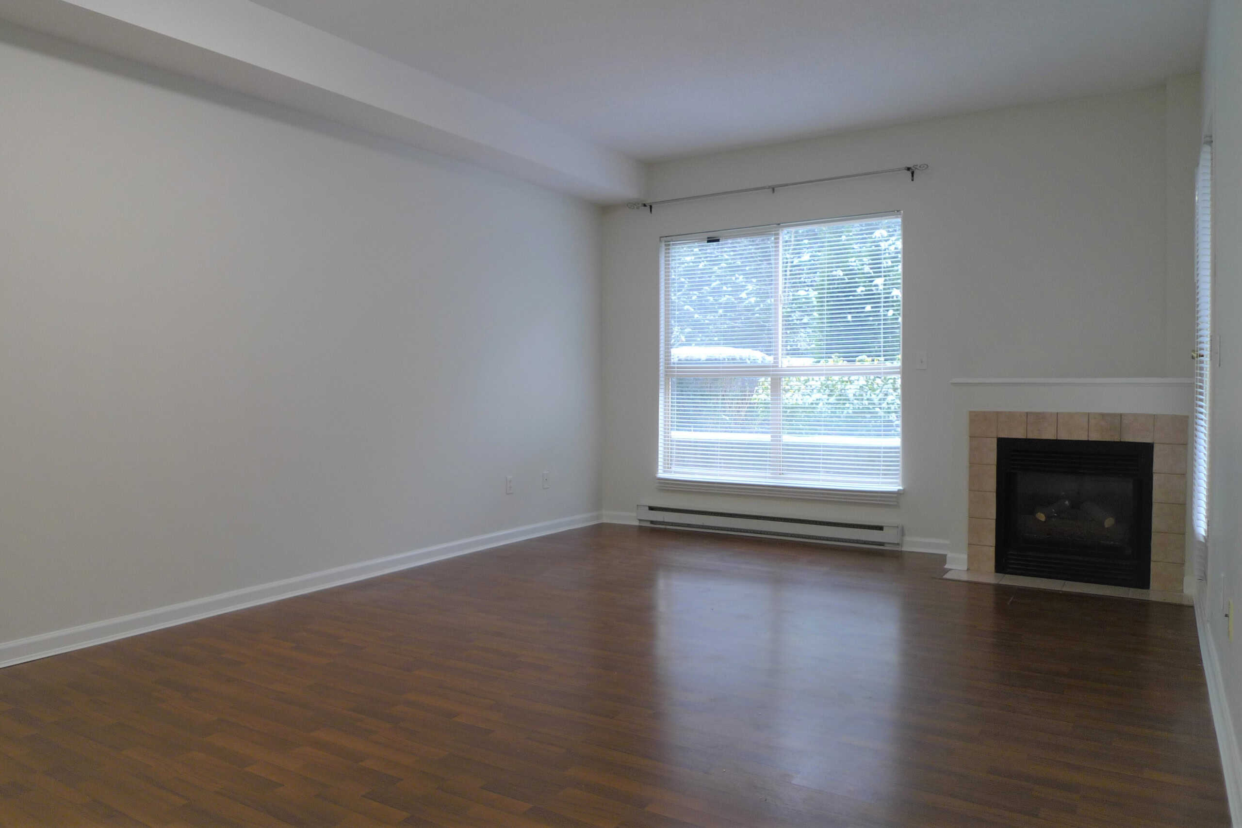 Bright living room with hardwood flooring, large window with blinds, and a cozy fireplace in a modern property listed by Orca Realty Inc.