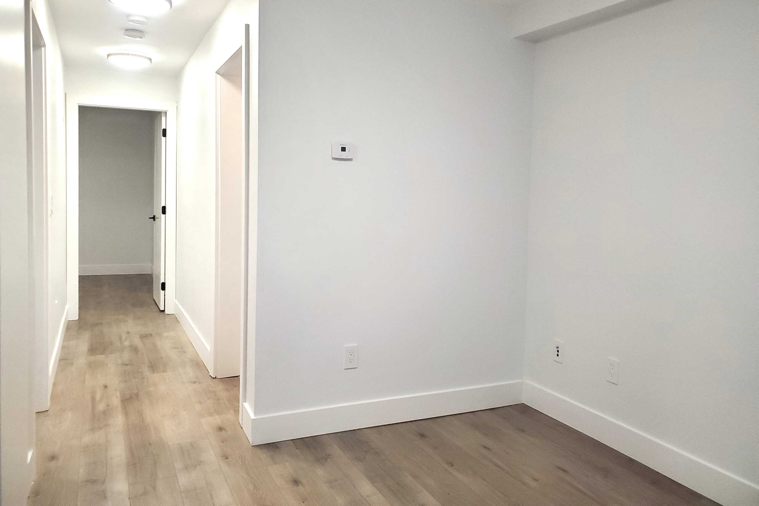 Bright empty bedroom interior with white walls and light wood flooring, showcasing modern residential space available through Orca Realty Inc. in Victoria, BC.