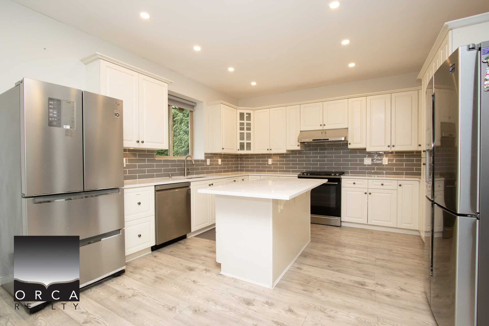 Bright modern kitchen with white cabinets, stainless steel appliances, grey subway tile backsplash, and a central island, ideal for Vancouver real estate buyers seeking stylish and functional homes.