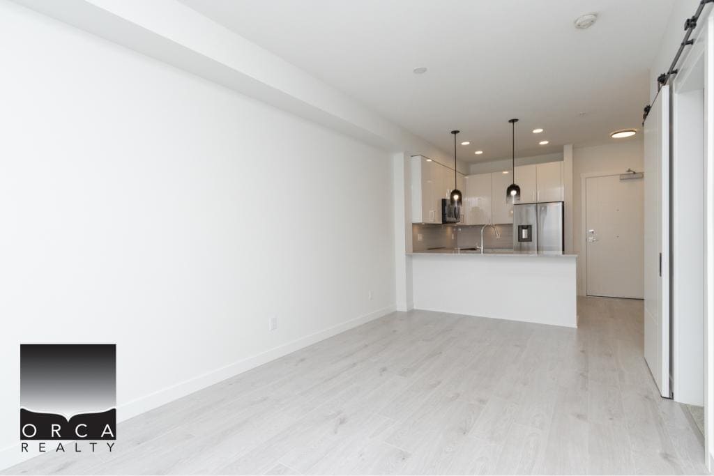 Modern minimalist kitchen and living space in a new condominium, featuring sleek white cabinetry, stainless steel appliances, and contemporary pendant lighting for optimal urban living.
