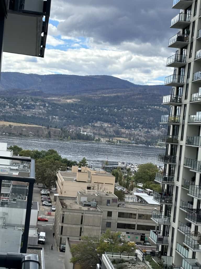Stunning waterfront view from a high-rise condo overlooking Okanagan Lake with mountains in the background, capturing the essence of upscale living and breathtaking scenery.