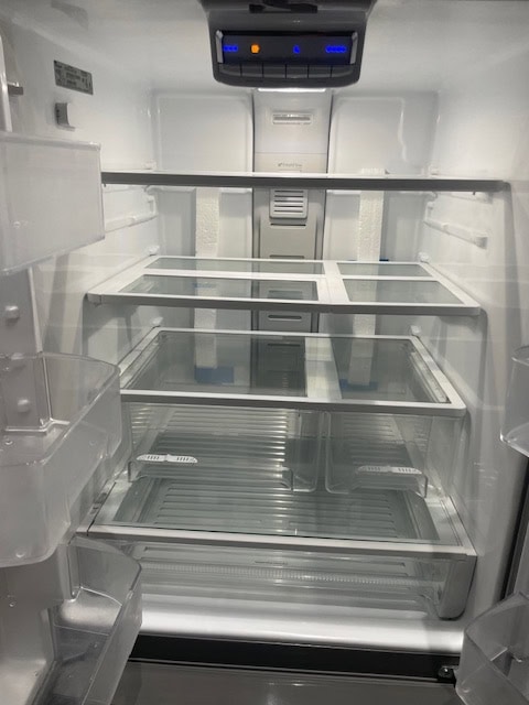 Empty modern refrigerator with glass shelves and LED lighting, showcasing high-end appliance features for luxury home listings.
