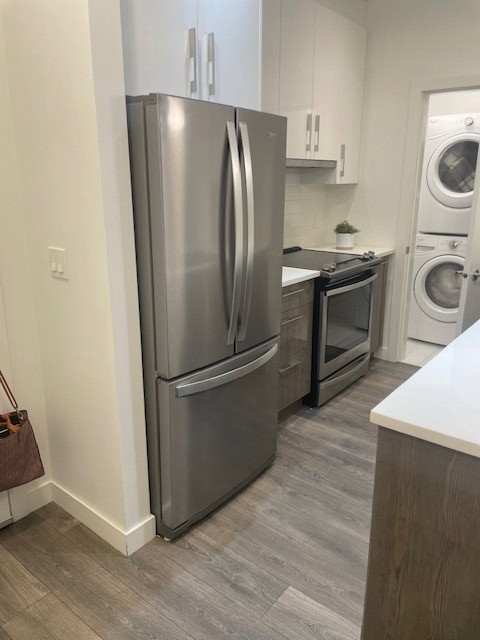 Stainless steel refrigerator in modern kitchen with white cabinets and laundry area in background, showcasing functional and stylish home appliance setup in Victoria, BC.