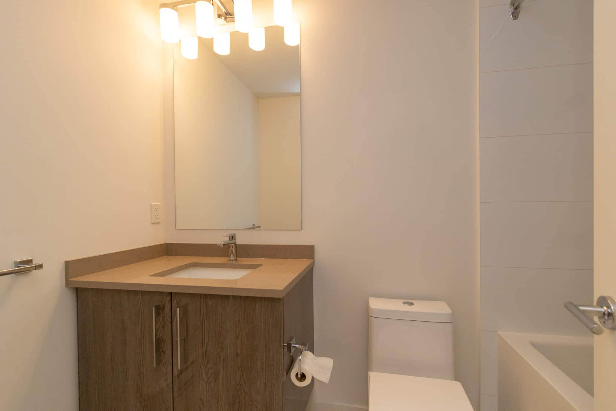 Modern bathroom with wooden vanity, beige countertop, bright lighting, and neutral wall colours, perfect for contemporary homebuyers interested in Vancouver real estate.