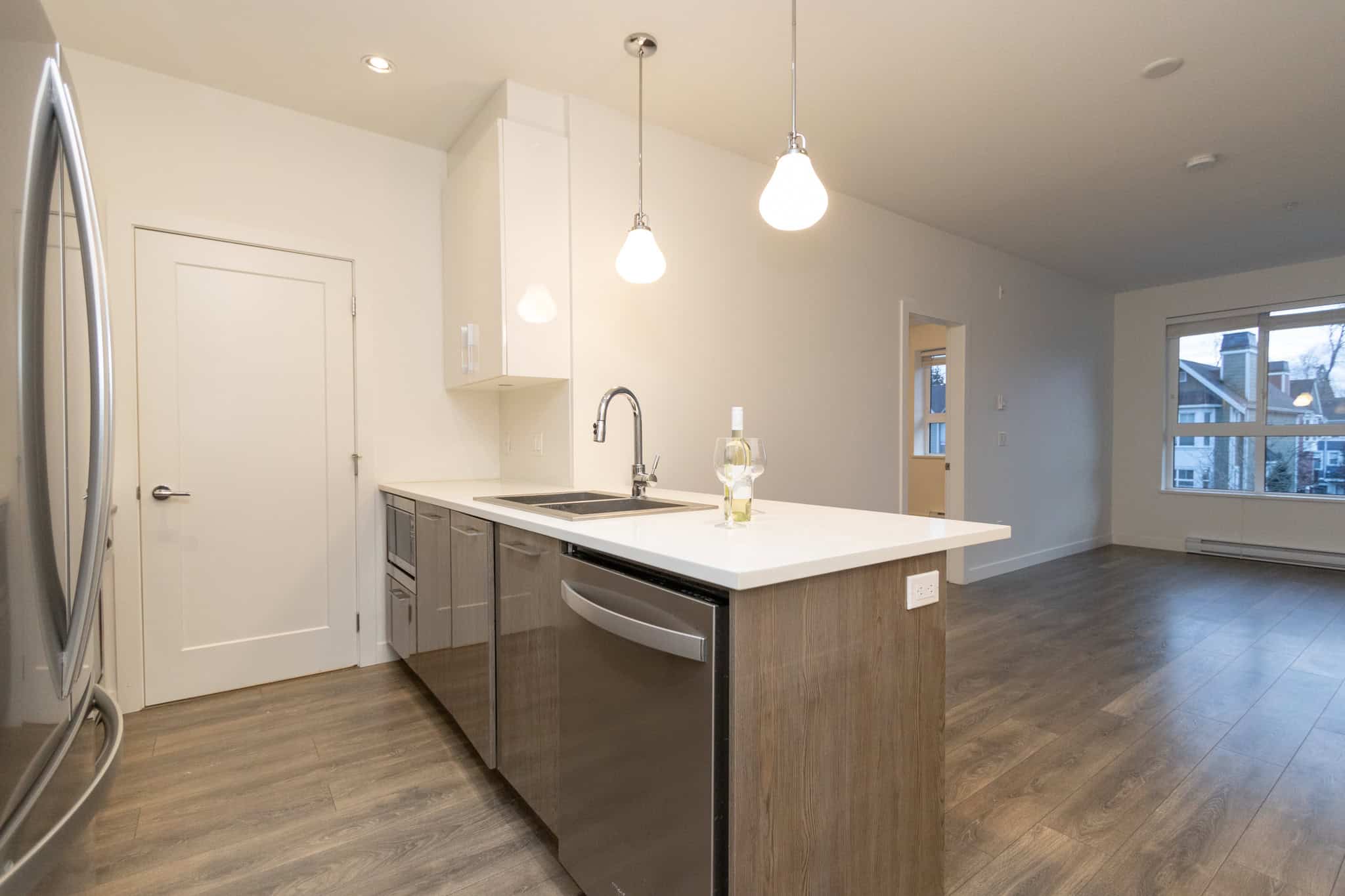 Modern kitchen with stainless steel appliances, white countertops, and hardwood flooring, in a bright open-concept living space for Vancouver Island real estate.