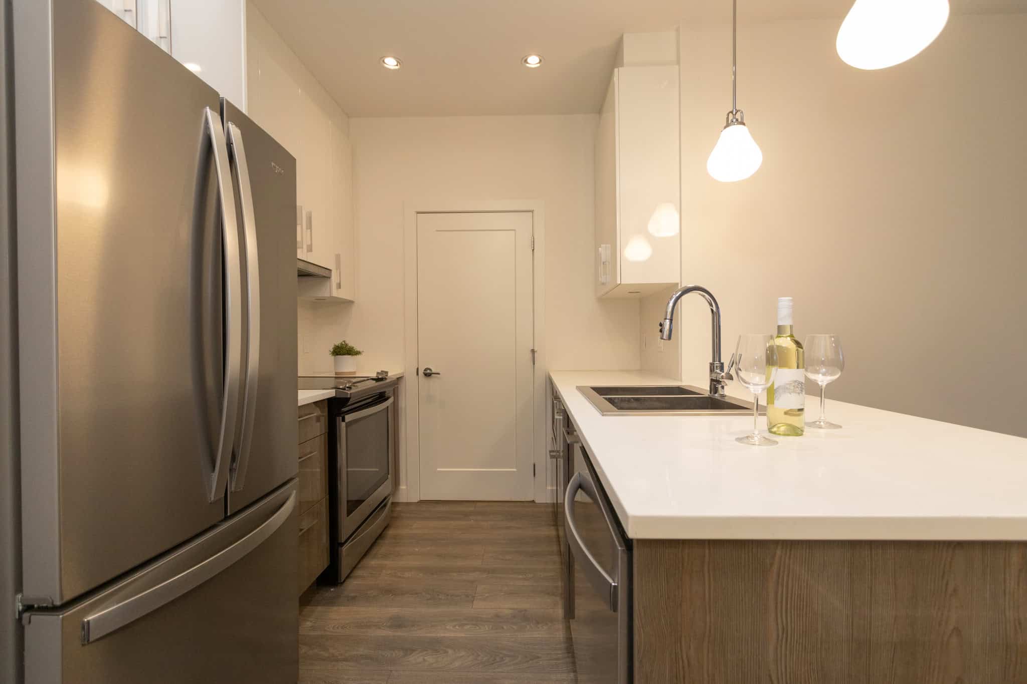 Modern stainless steel refrigerator and sleek kitchen appliances in a contemporary condo kitchen featuring white cabinetry, a quartz countertop, and pendant lighting, perfect for Vancouver real estate.