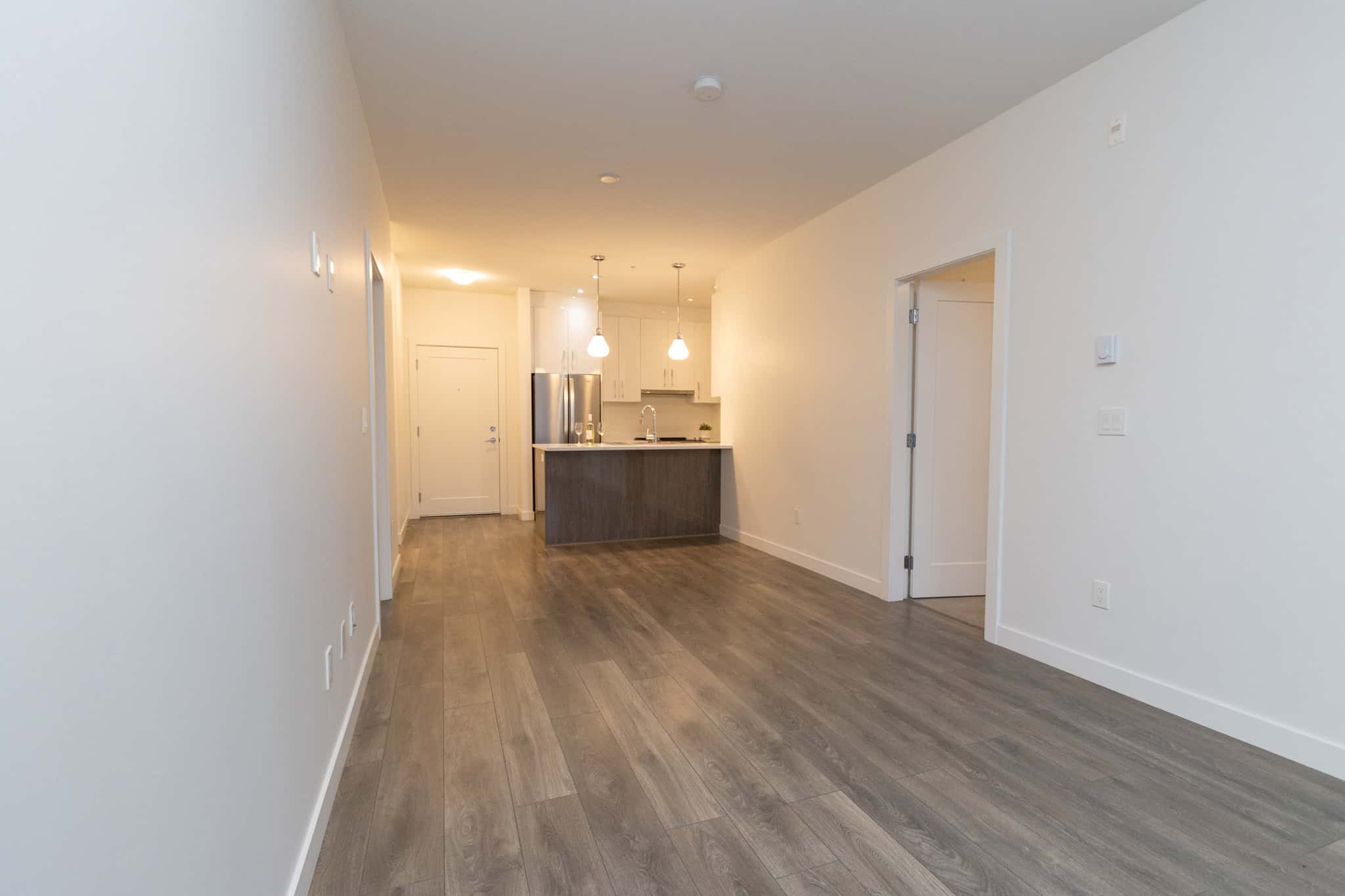 Spacious modern open-concept living area with hardwood flooring, leading to a sleek kitchen with stainless steel appliances and island, ideal for Vancouver Island real estate buyers.