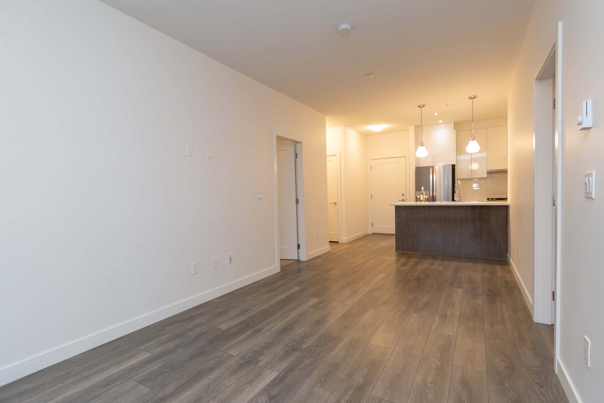 Spacious modern open-concept living area with hardwood floors and minimalist design, featuring a sleek kitchen with stainless steel appliances in a new residential property.