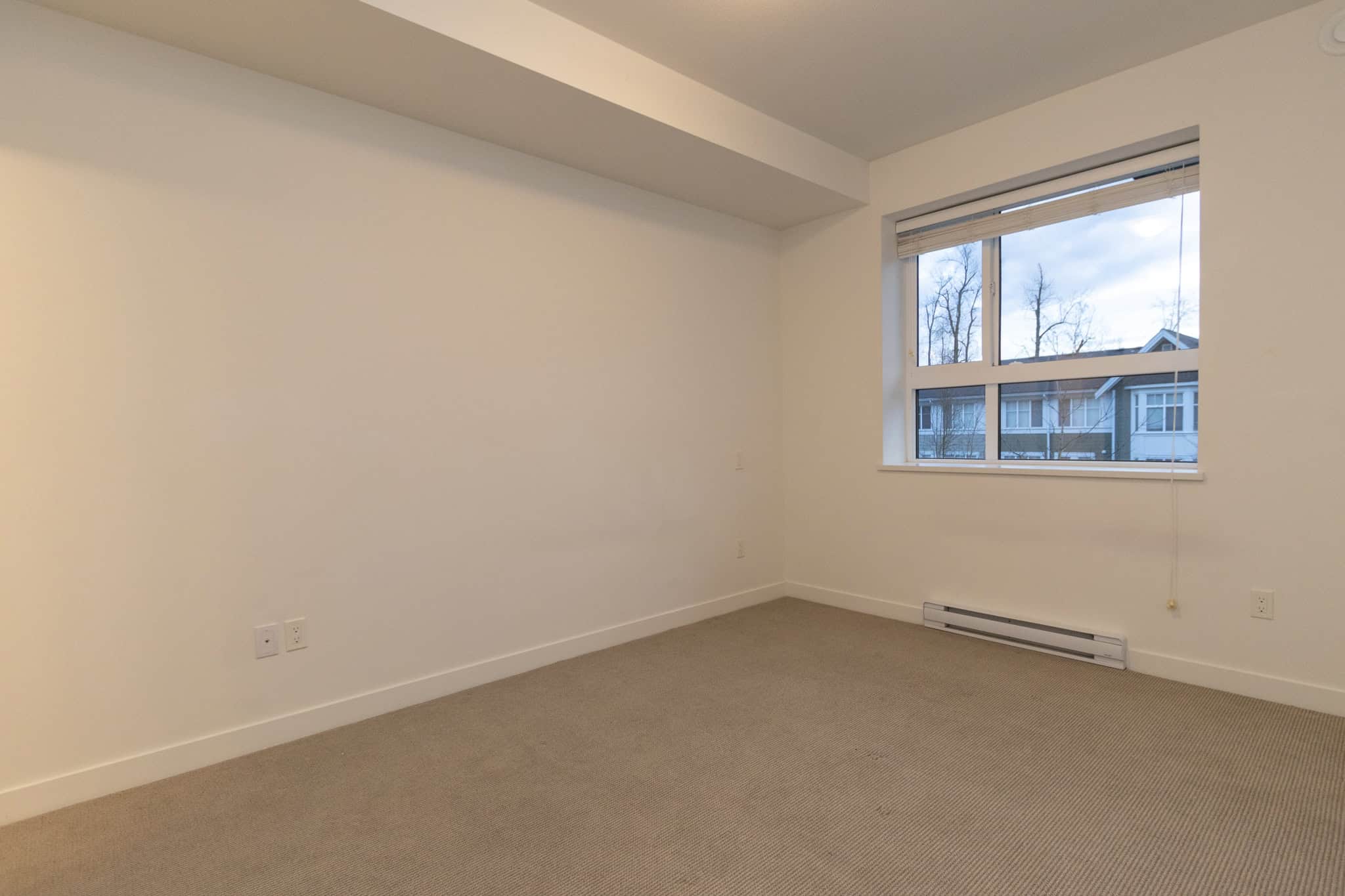 Bright empty apartment room with large window, neutral carpet, and white walls, ideal for Vancouver real estate investment or first-time homebuyers seeking a comfortable condo in BC.