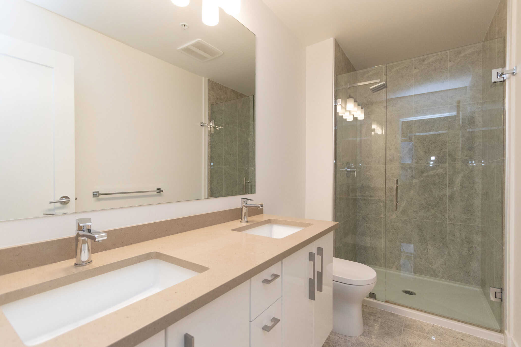 Modern bathroom with dual vanities, sleek fixtures, and a spacious glass-enclosed shower, showcasing upscale Vancouver real estate by Orca Realty Inc., ideal for luxurious home living.