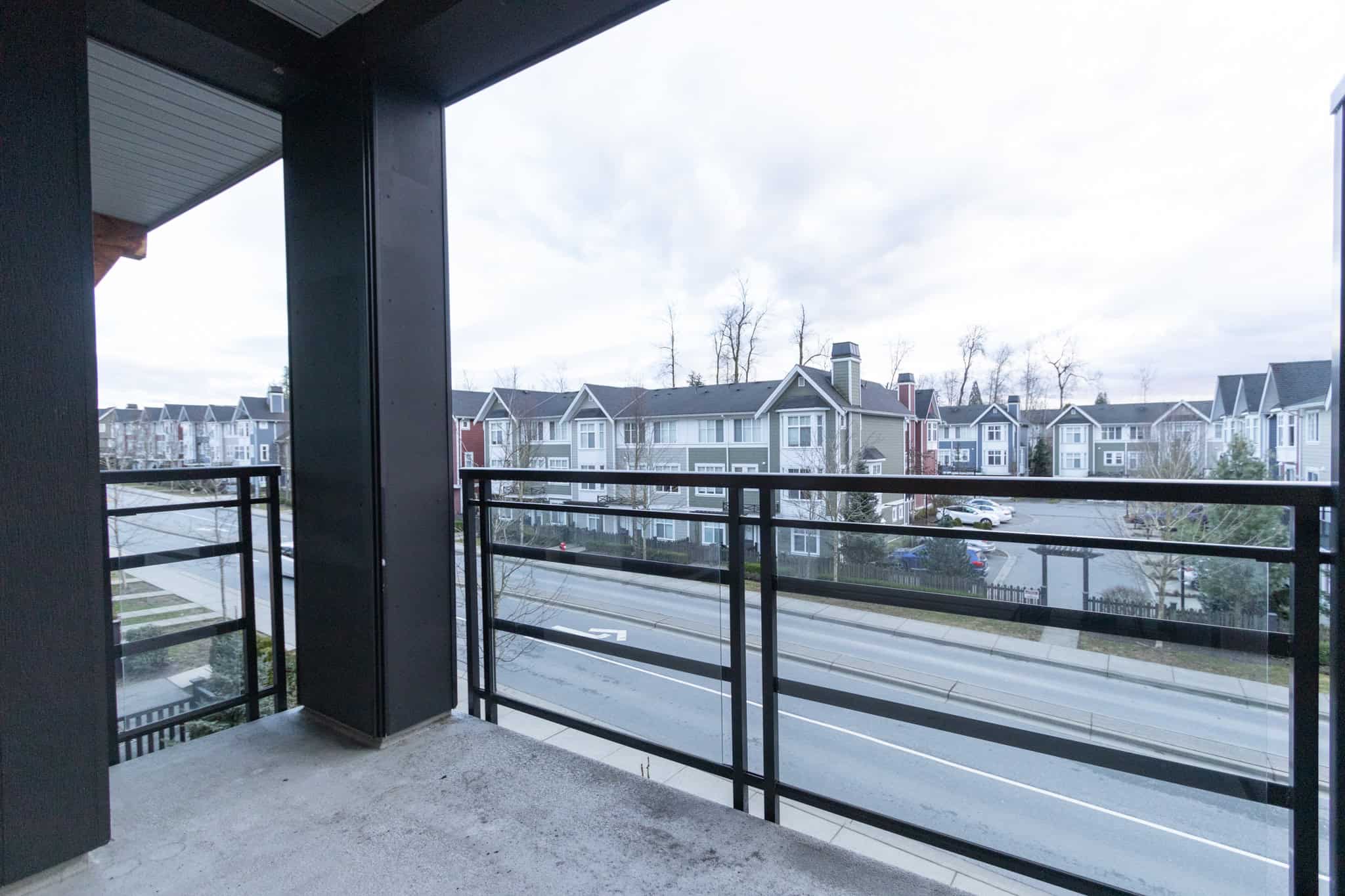 Modern balcony overlooking a residential neighbourhood with contemporary multi-family homes in a suburban setting, ideal for real estate buyers in Vancouver, BC, seeking new apartment listings.
