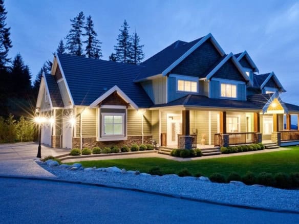 Gorgeous modern house with welcoming porch, situated in a scenic wooded area, illuminated at dusk, showcasing high-quality construction and prime real estate in BC.