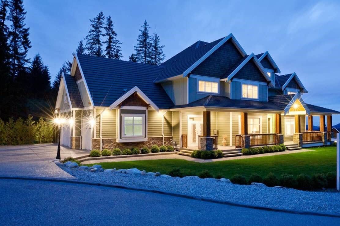 Gorgeous modern house with welcoming porch, situated in a scenic wooded area, illuminated at dusk, showcasing high-quality construction and prime real estate in BC.