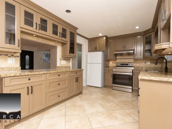 Spacious modern kitchen with granite countertops, beige cabinetry, stainless steel appliances, and tile flooring, perfect for family living and entertaining.