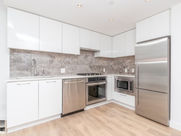 Modern white kitchen with stainless steel appliances, granite backsplash, and light wood flooring, ideal for Vancouver real estate listings.
