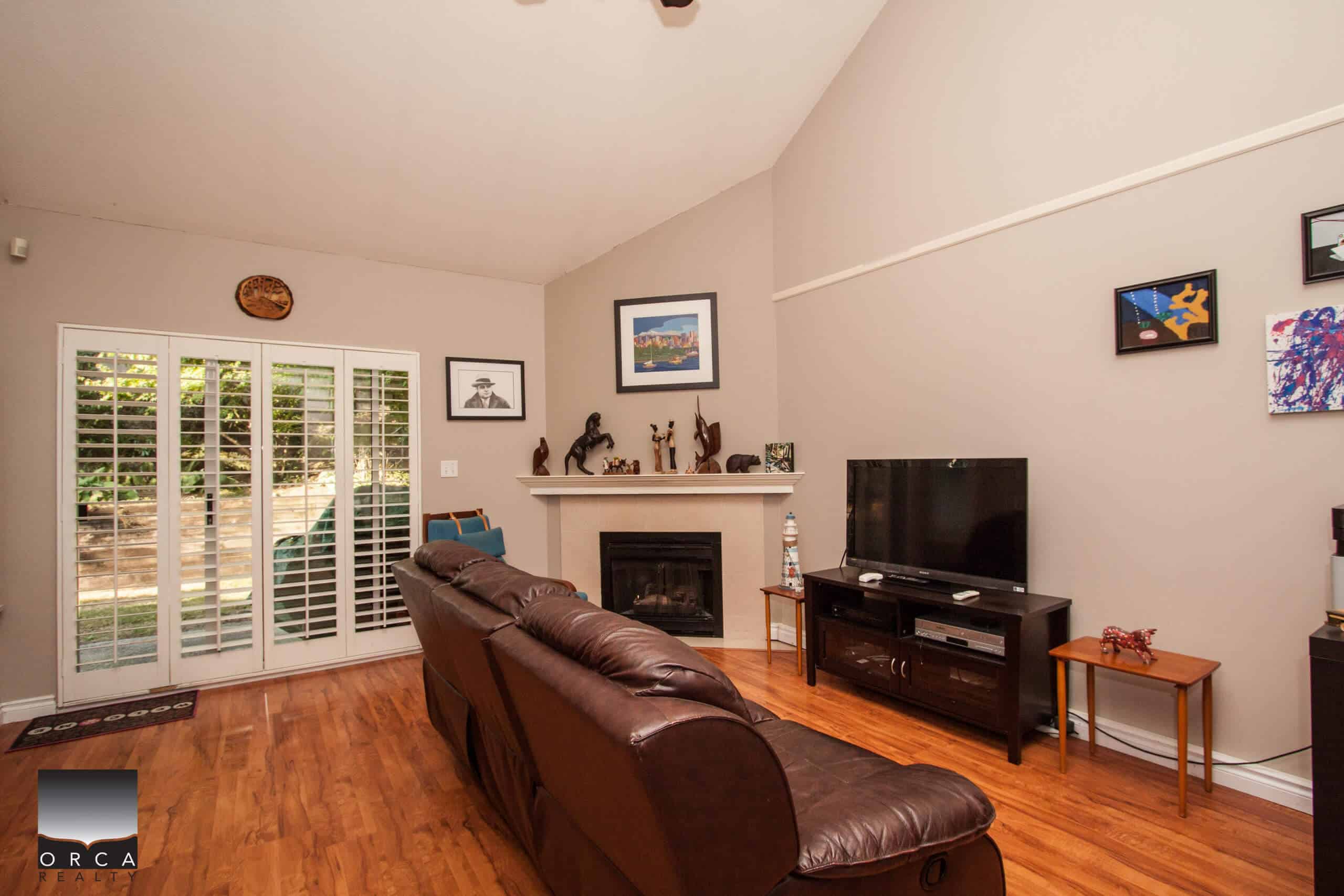 Cozy living room interior with fireplace, brown leather sofa, modern art, and natural light in a Vancouver home listed by Orca Realty Inc.