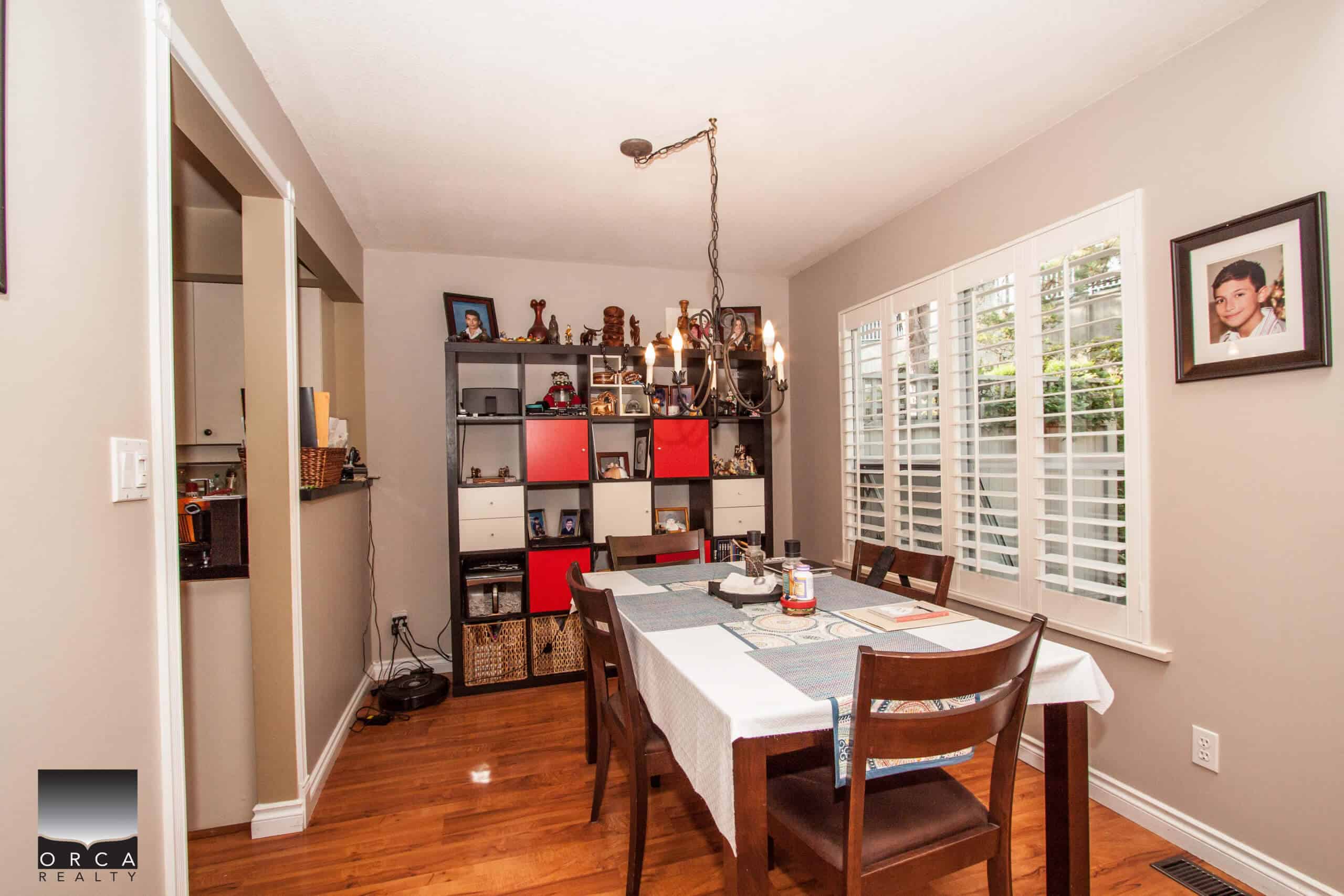 Spacious dining room with hardwood floors, modern decor, and large windows with white shutters, perfect for family gatherings and entertaining guests.