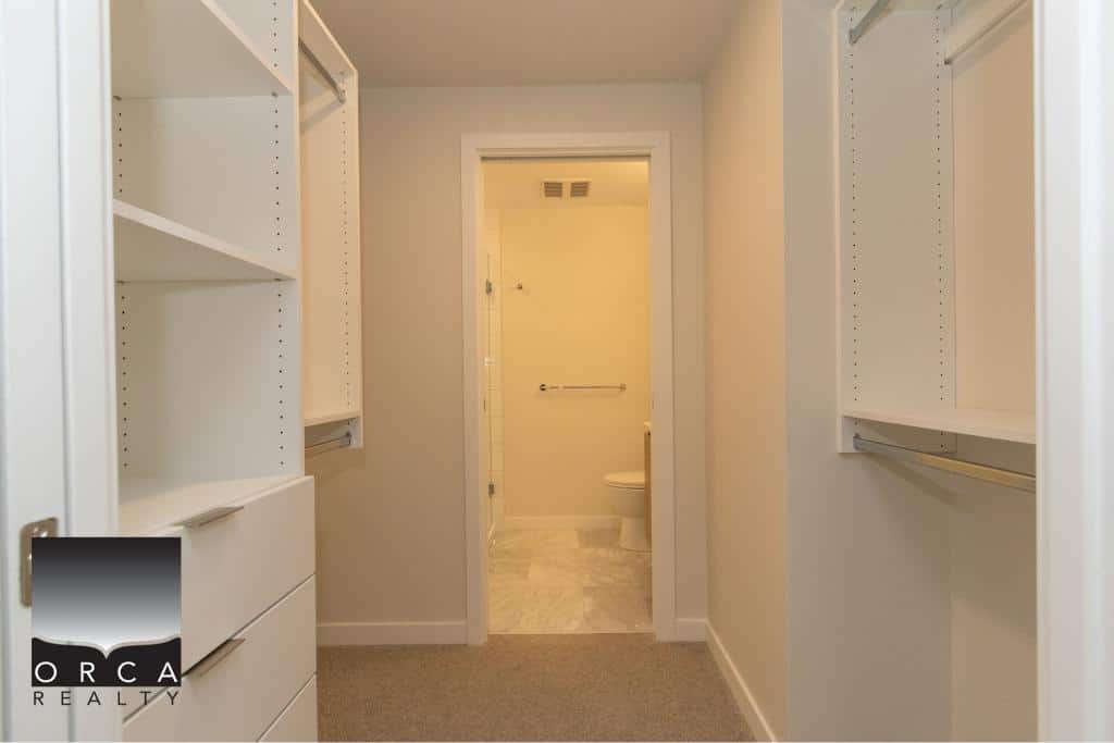 Modern walk-in closet with built-in shelves and storage space, leading to a bathroom, perfect for Vancouver home buyers seeking organized interiors.