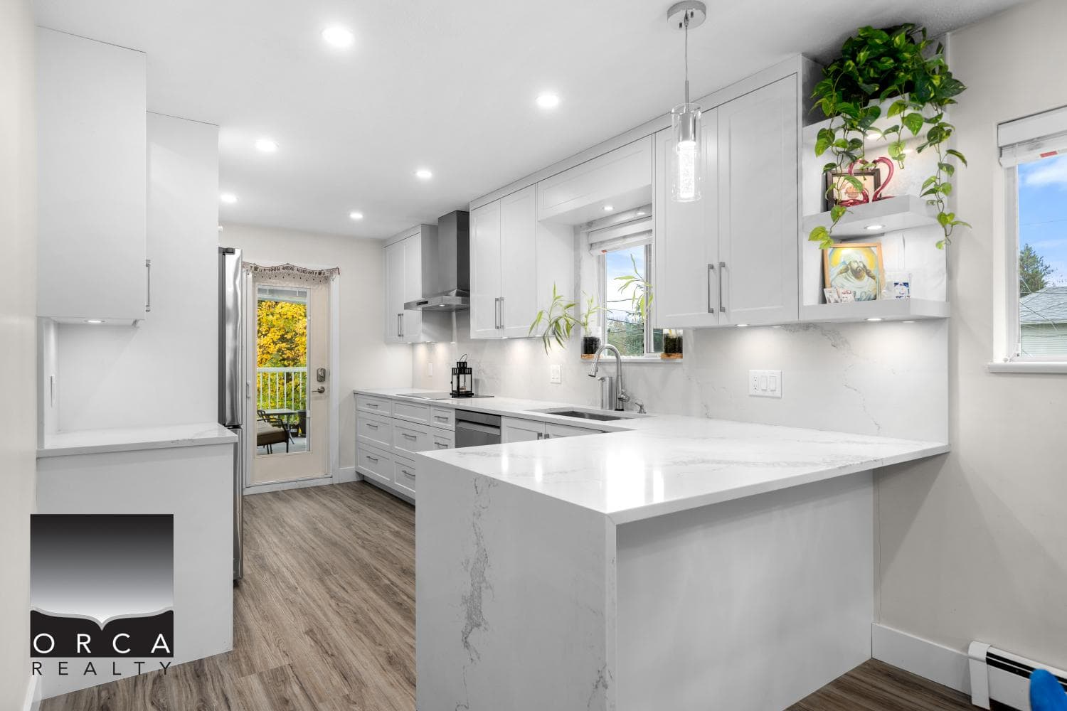 Bright modern kitchen with white cabinetry, marble countertops, stainless steel appliances, and large windows providing natural light - perfect for homes in Vancouver Island.