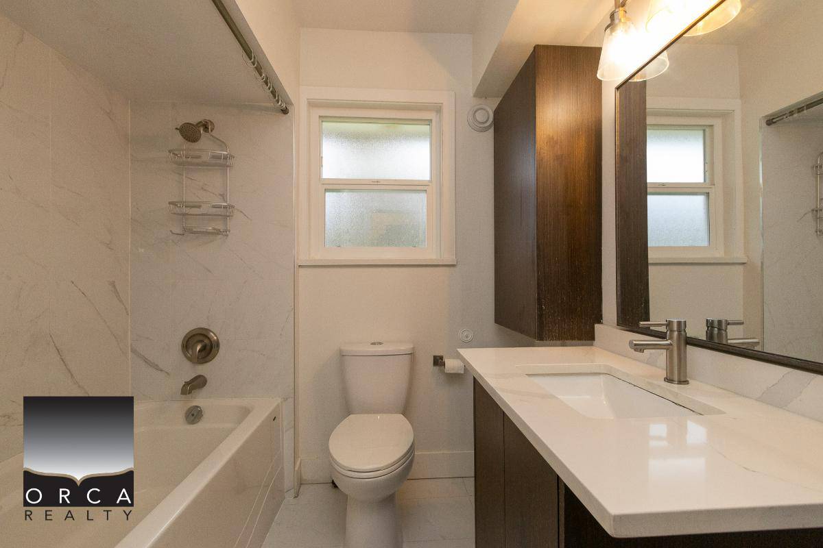 Modern bathroom with bathtub, white fixtures, dual windows, and dark wood cabinetry in a contemporary Orca Realty Inc. listings. Perfect for buyers seeking stylish Vancouver Island homes.