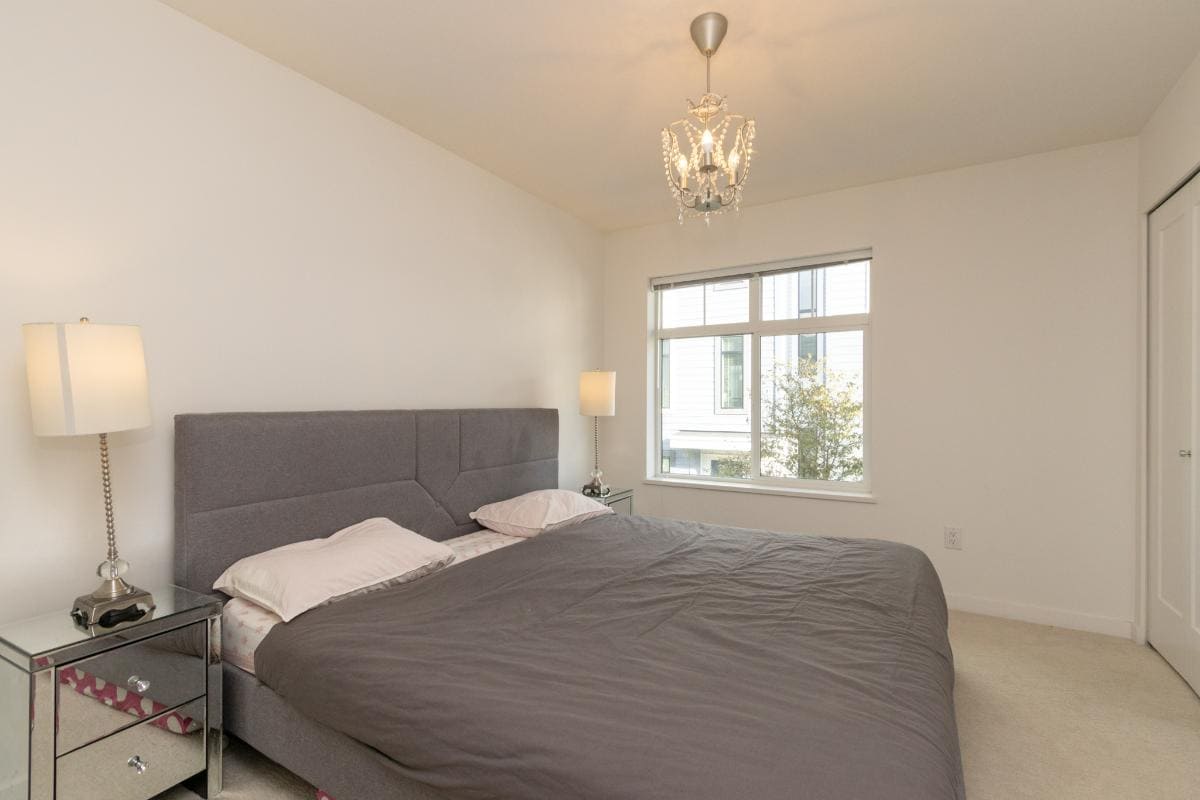 Bright modern bedroom with large window, grey upholstered bed and elegant chandelier, perfect for contemporary Vancouver living.