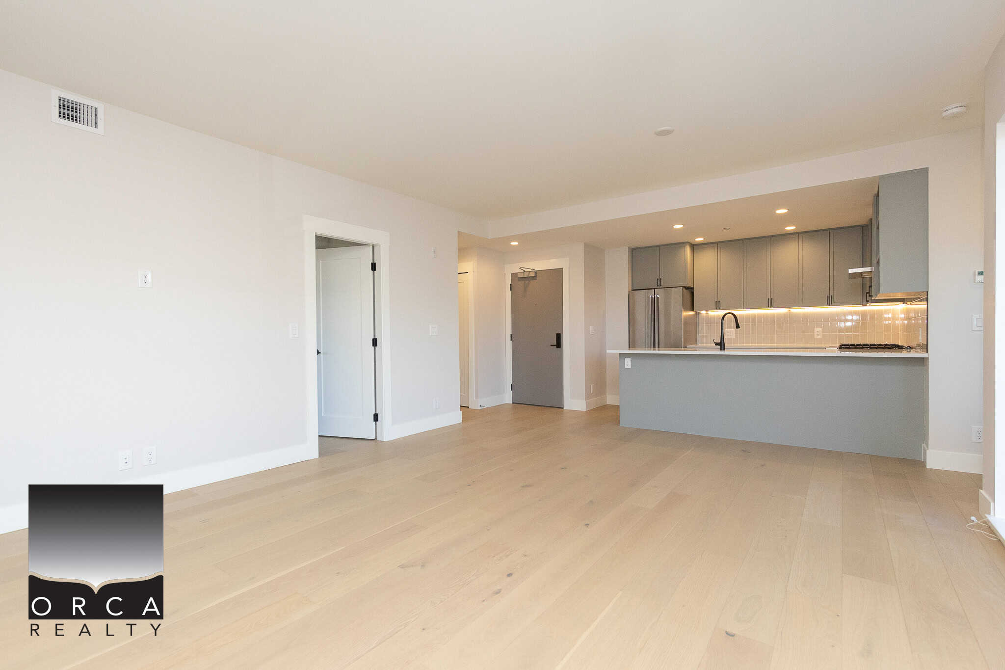 Bright modern kitchen and open living space in a contemporary condo, featuring sleek gray cabinets, minimalist design, and natural light, ideal for Vancouver Island real estate buyers.