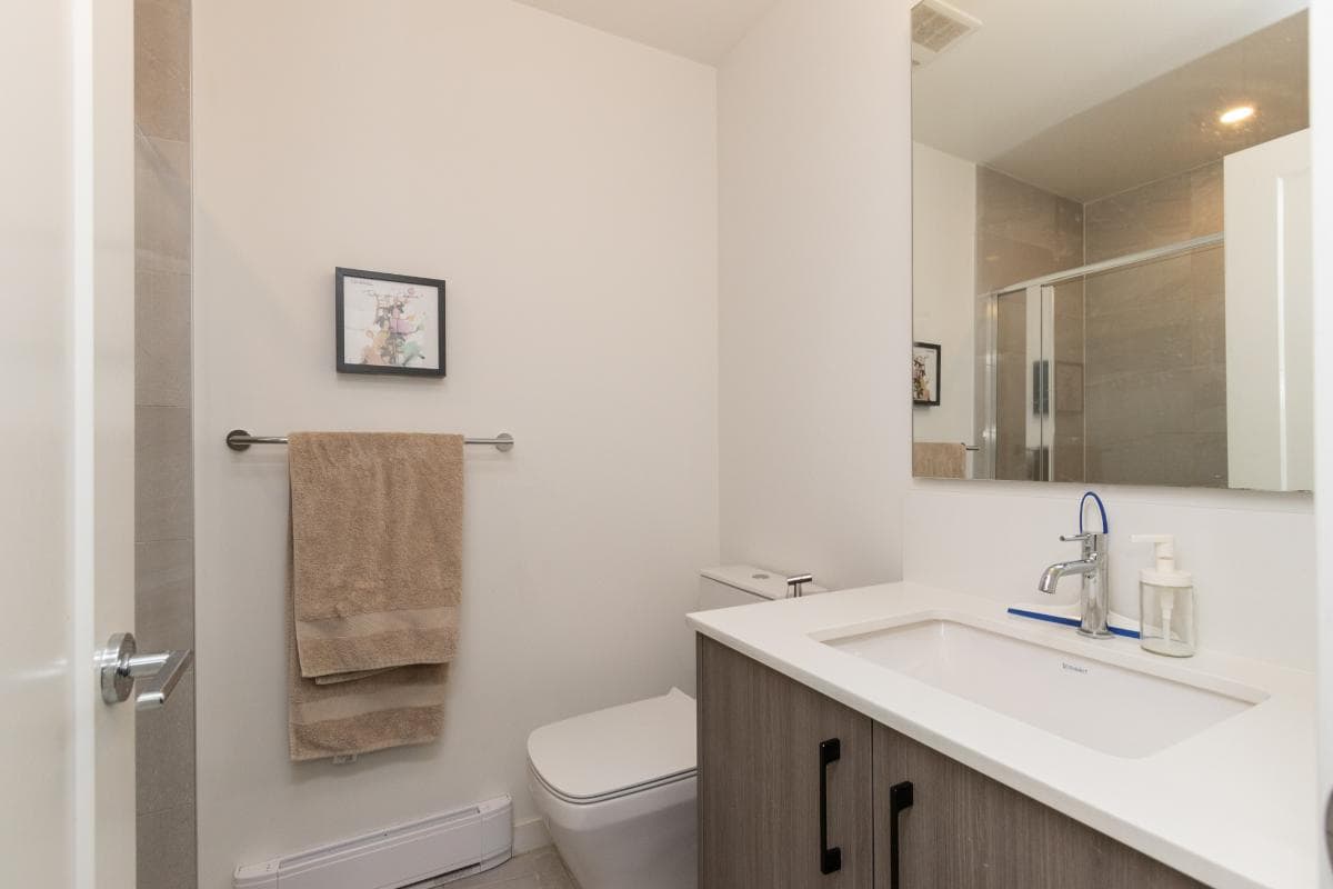 Modern bathroom with white walls, beige towels, sleek vanity with countertop sink, large mirror, and glass shower enclosure, in a contemporary Vancouver home for sale by Orca Realty Inc.