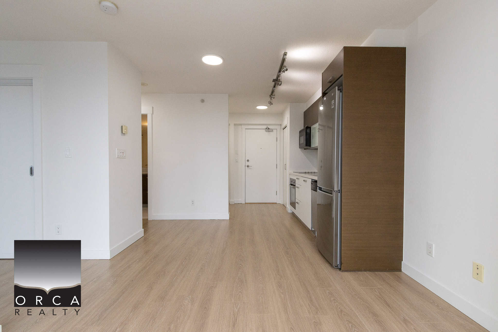 Modern open-concept kitchen with stainless steel appliances, light wood flooring, and minimalist white walls, perfect for Vancouver condo living.