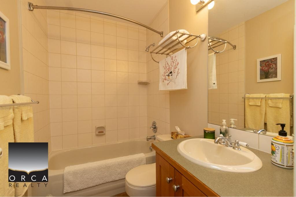 Bright bathroom with bathtub, beige tiles, and wooden vanity in a modern home for sale by Orca Realty Inc. in BC. Perfect for buyers seeking a comfortable, well-maintained property.